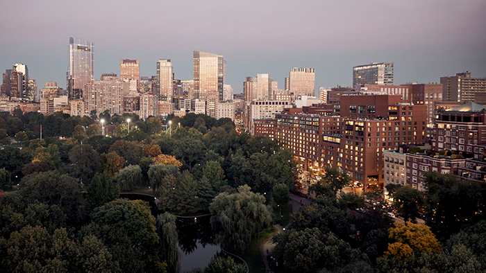The exterior of the Four Seasons Hotel Boston with a lush park in the foreground and the city skyline in the background.