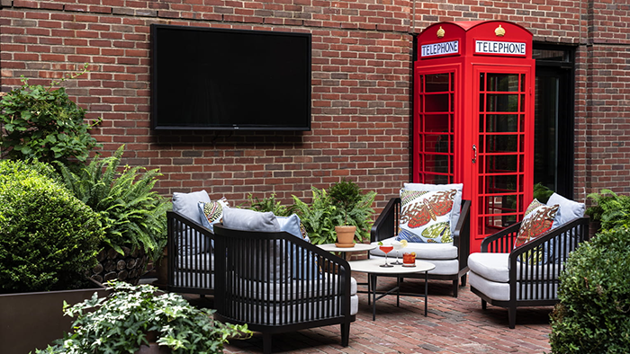 The courtyard at the Four Seasons Hotel Boston, with brick walls and floors as well as plenty of greenery and seating. Notably, a bright red telephone booth is also present.