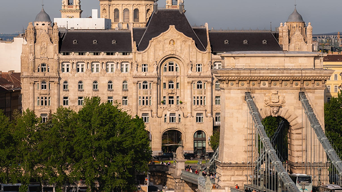 The ornate exterior of the Four Seasons Hotel Gresham Palace Budapest, with an equally intricate bridge located directly in front of the historic hotel.