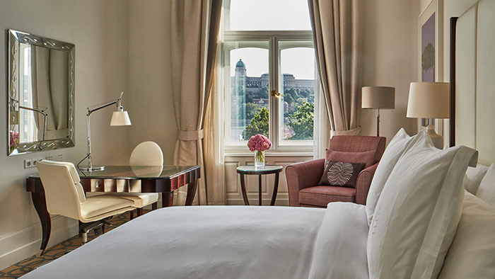 A guest room at the Four Seasons Hotel Gresham Palace Budapest with a large, cozy-looking bed and a window overlooking the River Danube.