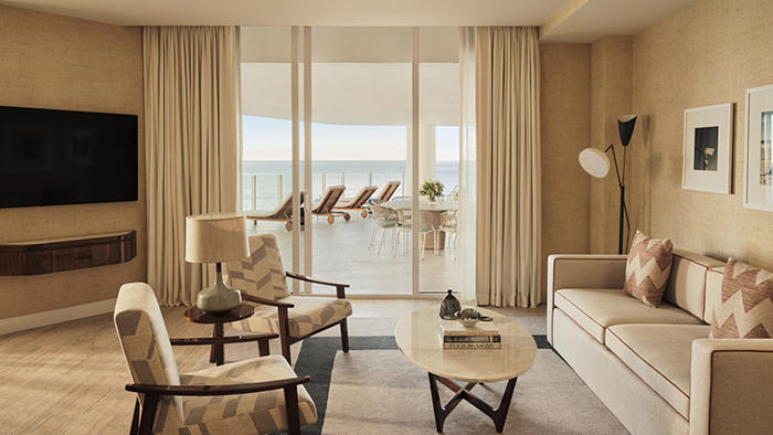 A suite at the Four Seasons Hotel and Residences Fort Lauderdale with a sliding glass door opening up to a large balcony with lots of seating.