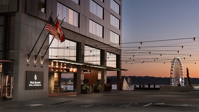 The exterior of the Four Seasons Hotel Seattle. A ferris wheel is visible in the background, with Elliott Bay just behind it.