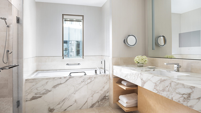 A guest bathroom at the Four Seasons Hotel Seattle. The countertop and bathtub are both marble, and a small arrangement of fresh flowers sits to the left of the sink.