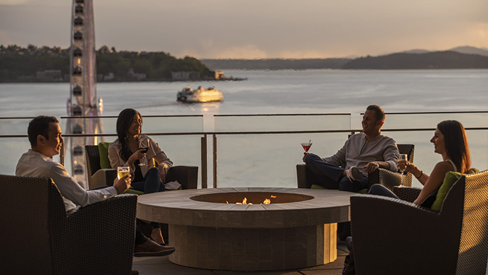 Four guests enjoy drinks while sitting around an outdoor firepit overlooking Elliott Bay at the Four Seasons Hotel Seattle.