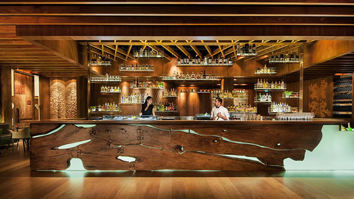 One of the bars at the Four Seasons Hotel Sydney. Two bartenders are seen working, surrounded by the bar's earthy decor.