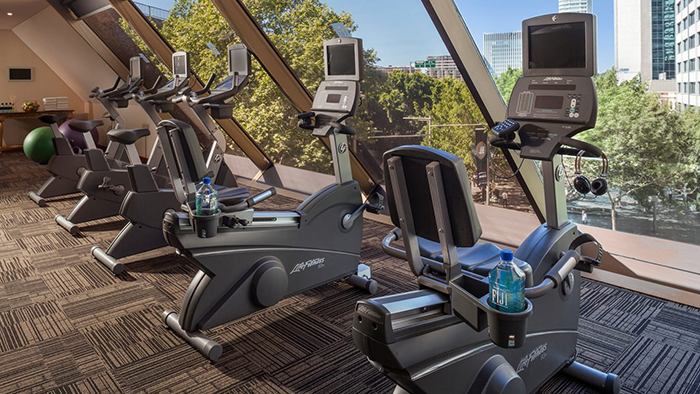 The fitness center at the Four Seasons Hotel Sydney. Stationary bikes are set up facing a window overlooking the city.