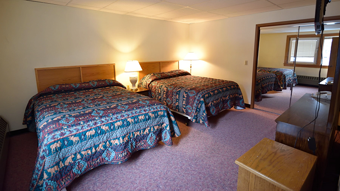The inside of a guest room at the Anchor Inn Hotel. There are two queen beds, each adorned with a comforter featuring depictions of classically Alaskan animals.