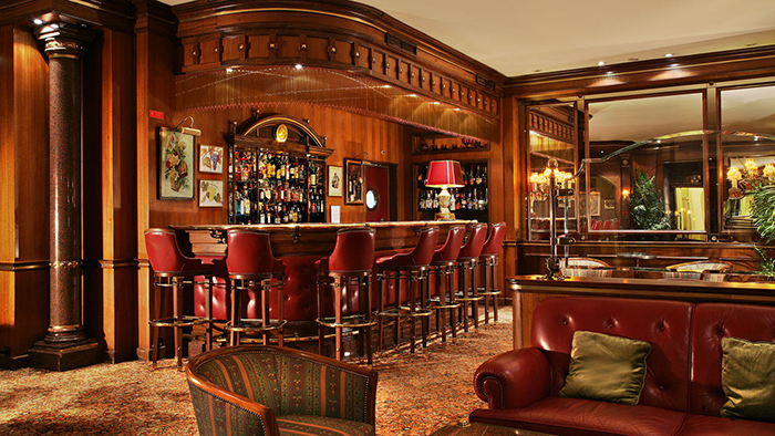 A bar inside the Avenida Palace hotel in Lisbon, Portugal. The decor features an abundance of wood that's complemented by red leather seating.