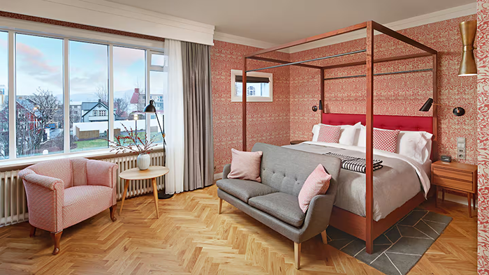 A guest room at the Canopy by Hilton Reykjavik City Centre. The walls are covered in bold patterned wallpaper, and there's a lovely neighborhood view through the window.