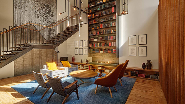 A common area with seating at the Canopy by Hilton Reykjavik City Centre. Many, many books are displayed on a shelf that's far too tall for any human to reach the top without assistance.