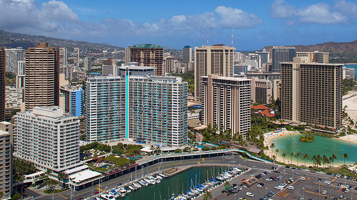 The exterior of the Castle Ilikai Tower Hotel in Honolulu, Hawaii. The hotel sits on the waterfront just past a line of docked boats.