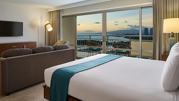 A guest room at The Castle Ilikai Tower Hotel. A picturesque Hawaiian view is visible beyond the balcony.