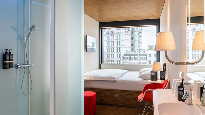 A guest room inside the citizenM Rotterdam hotel. The Rotterdam cityscape is visible through a window.
