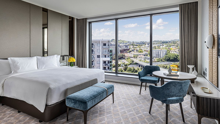 A guest room at the Cordis, Auckland hotel. A lovely view of some buildings and greenery is seen through the room's large window.