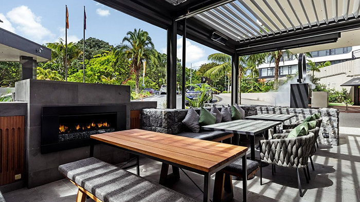 An outdoor seating area at the Cordis, Auckland hotel. A lit fireplace is visible on the left side of the patio.