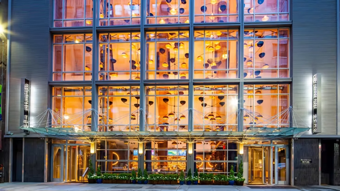 An exterior shot of the Crowne Plaza HY36 Midtown Manhattan hotel. Hanging light fixtures that are several stories tall can be seen through the glass.
