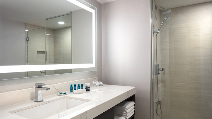 A guest bathroom at Delta Hotels by Marriott Vancouver Downtown Suites. There's an LED light surrounding the mirror for increased reflection visibility.