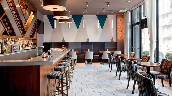 The bar area inside of the Element Harrison Newark hotel. The back wall is decorated with an abstract geometric design.