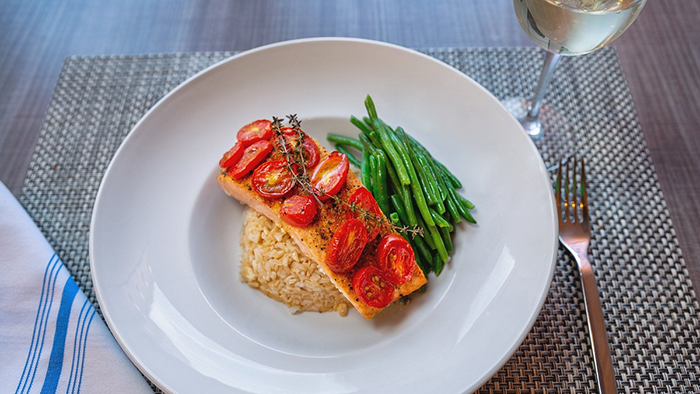 A meal prepared by the Element Harrison Newark hotel kitchen. A piece of salmon is served with brown rice, cherry tomatoes, and asparagus.