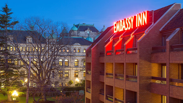 The outside of the Embassy Inn Hotel in Victoria, British Columbia. The building's brick facade is accented by a large flourescent sign.