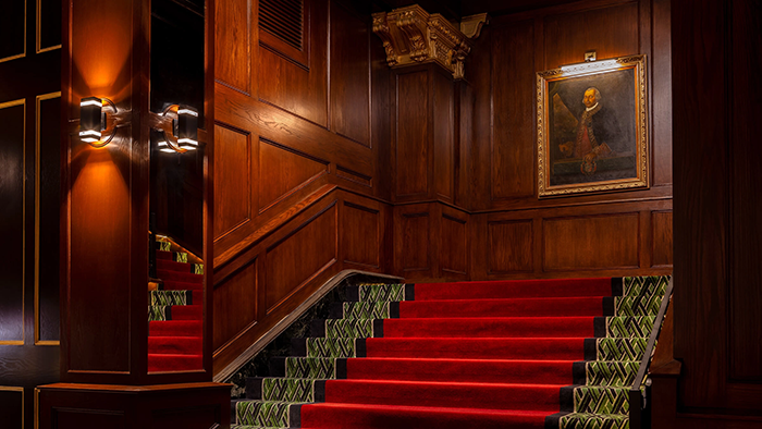 A staircase inside the Grand Galvez hotel in Galveston, Texas. An old portrait of a regally dressed man hangs above the top of the stairs.