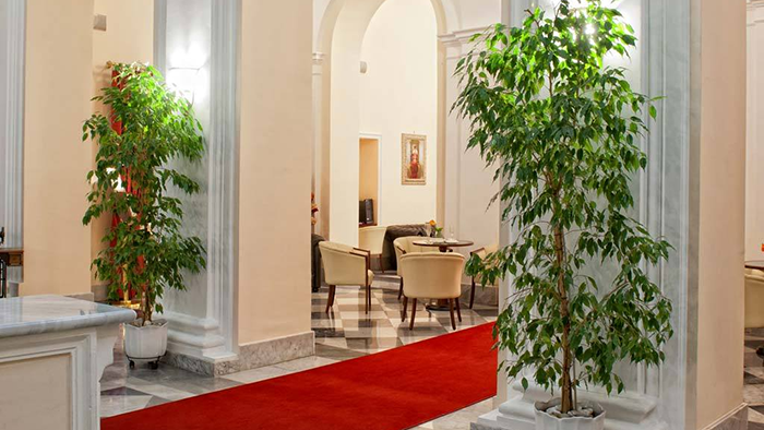 The lobby of the Hotel San Giorgio in Civitavecchia, Italy. A bright red carpet is laid across a floor covered in black and white checkered tile.