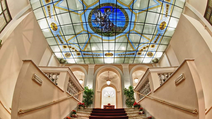 A staircase inside the Hotel San Giorgio. The ceiling above the stairs is decorated by a stainless glass depiction of a man riding a horse and wearing a suit of armor.