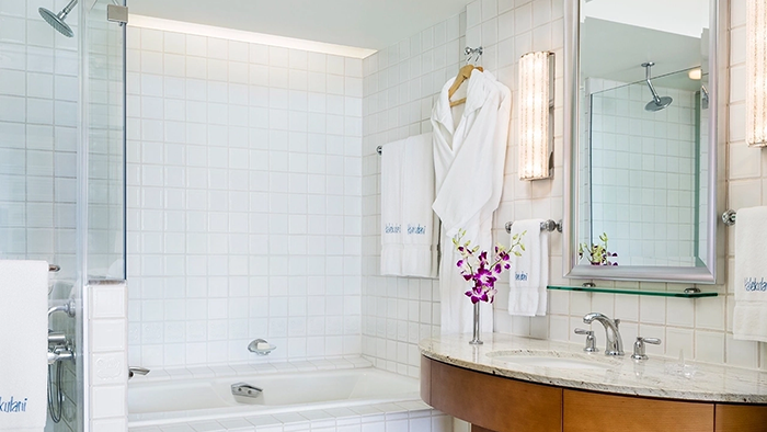 A guest bathroom at the Halekulani Hotel in Honolulu, Hawaii. Two bathrobes as well as several Halekulani-branded towels are hanging from the wall.