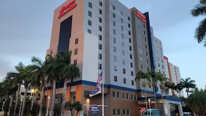 The exterior of Hampton Inn & Suites by Hilton Miami Airport South Blue Lagoon. In classic Florida fashion, rows of palm trees decorate the property.