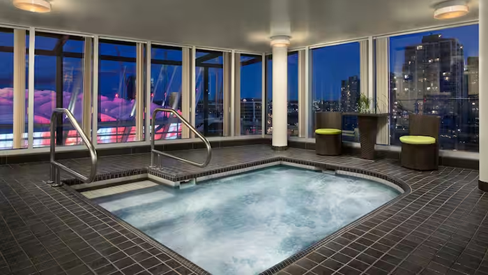 A hot tub inside the Hampton Inn & Suites by Hilton Vancouver-Downtown hotel. The Vancouver cityscape is visible through the window.
