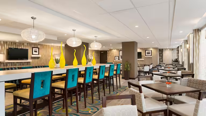A restaurant inside the Hampton Inn & Suites by Hilton Vancouver-Downtown hotel. A long table in the center of the room has four yellow sculptures sitting on top of it.