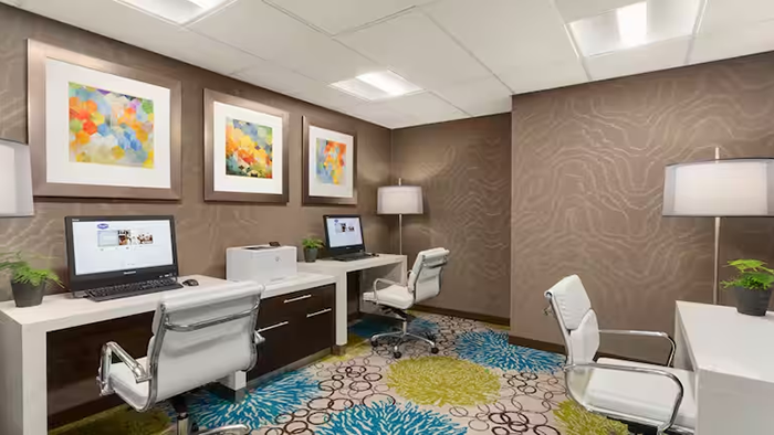 A small workspace at the Hampton Inn & Suites by Hilton Vancouver-Downtown hotel. Three desks are shown with computers available for public use.