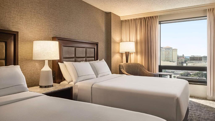A guest room at the Hilton Tampa Downtown hotel. Two beds, a chair, a bedside table, and two lamps are visible.
