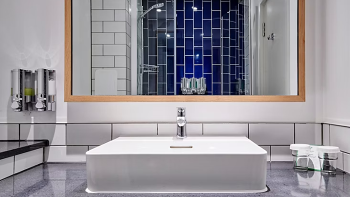 A guest bathroom inside the Holiday Inn Southampton, an IHG Hotel. The shower walls are lined with vibrant blue tile.