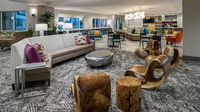A common area with seating and a unique chrome coffee table inside the Home2 Suites by Hilton Cape Canaveral Cruise Port hotel.