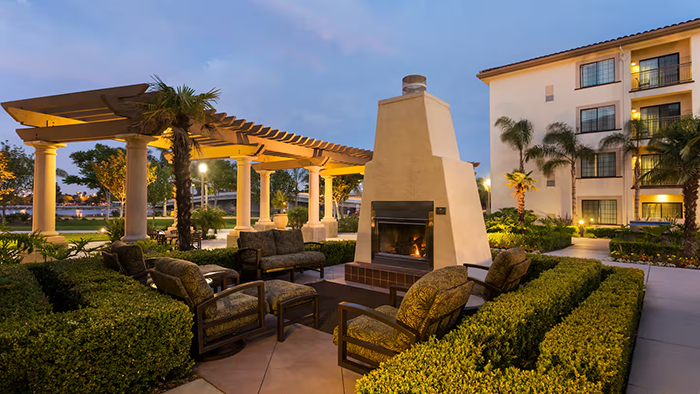 An outdoor seating area at the Homewood Suites by Hilton San Diego Airport-Liberty Station hotel. Seating and well-trimmed hedges surround a lit fireplace.