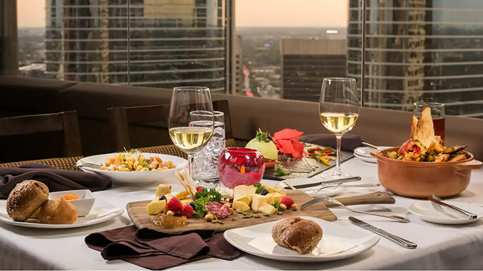 A meal served at the Hyatt Regency Houston hotel. Two glasses of white wine and several delicious-looking dishes are pictured with a view of downtown Houston in the background.