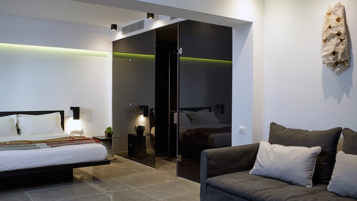 A guest room at in[n]Athens hotel featuring a large bed, a sofa, and a sliding door leading to the bathroom.