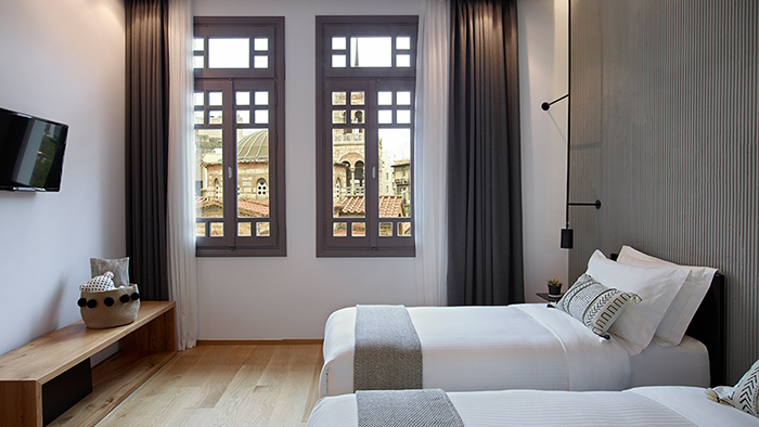 A guest room at in[n]Athens hotel featuring two twin beds and a window with a view of a historic church.
