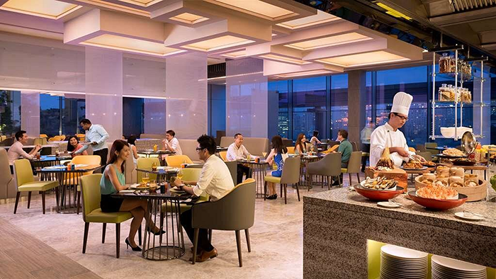 A restaurant inside the JEN Singapore Orchardgateway Hotel by Shangri-La. A man in a chef's uniform is pictured setting out some pastries.