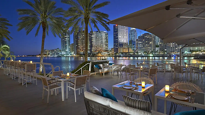 An outdoor restaurant at the Miami Mandarin Oriental. The sun has set, and the Miami skyline is lit up.