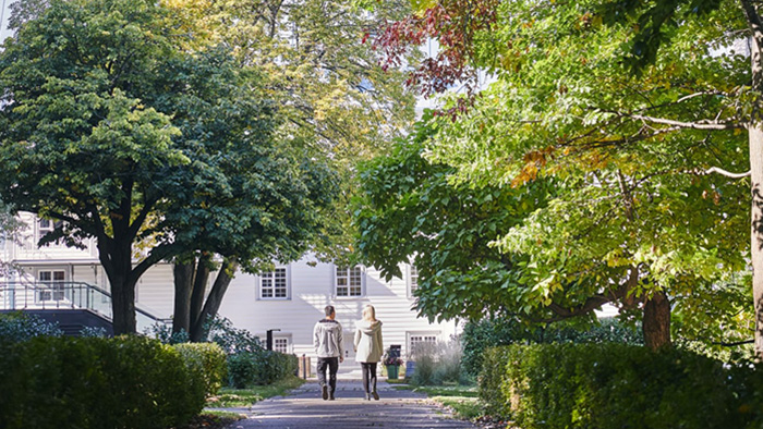 Two people go for a walk through the grounds at Le Monastre des Augustines. The pathway is lined with beautiful trees.