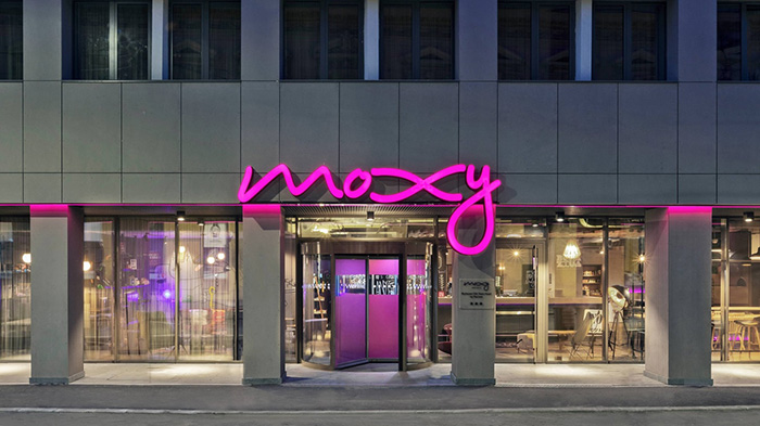The outside of the Moxy Hotel in Old Town Bucharest, Romania. The hotel's bright pink logo is prominently displayed.
