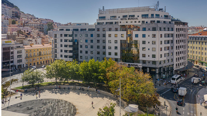 An exterior image of the Hotel Mundial in Lisbon, Portugal. A park with a fountain is visible in the foreground.