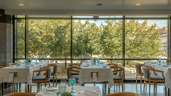 A restaurant inside the Hotel Mundial in Lisbon, Portugal. A row of trees is visible through the restaurant's large windows.