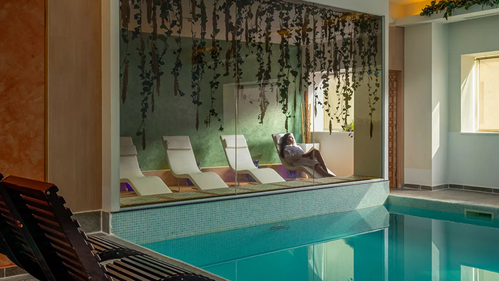 The indoor pool at Novotel Bucharest City Centre. A woman is seen lounging on a chair behind a large glass window.