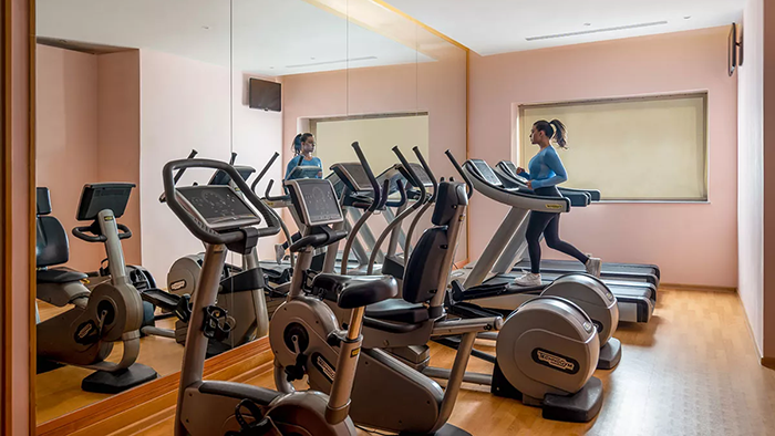 The hotel fitness center at Novotel Bucharest City Centre. A woman wearing her hair in a ponytail is seen running on a treadmill.