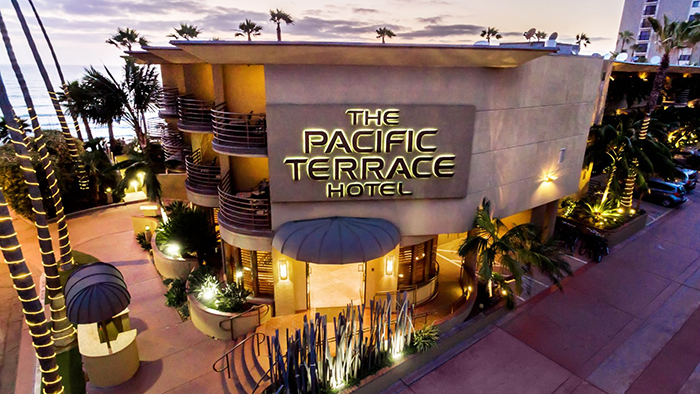 An exterior image of the Pacific Terrace Hotel in San Diego, California. The hotel's logo is prominently featured above the front door.