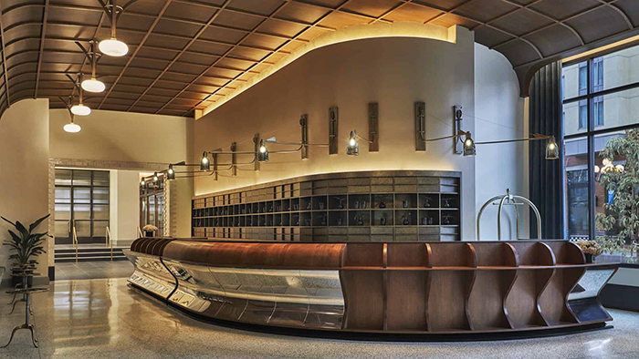 The front desk at Pendry San Diego. The left side of the counter features reflective chrome detailing on the underside.