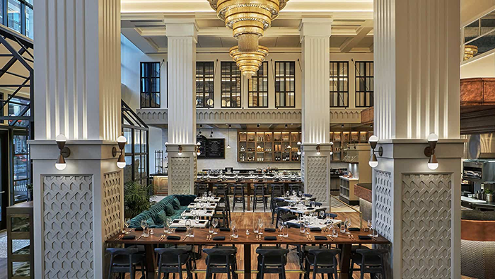 A restaurant inside Pendry San Diego. Two golden chandeliers hang from the room's tall ceiling.